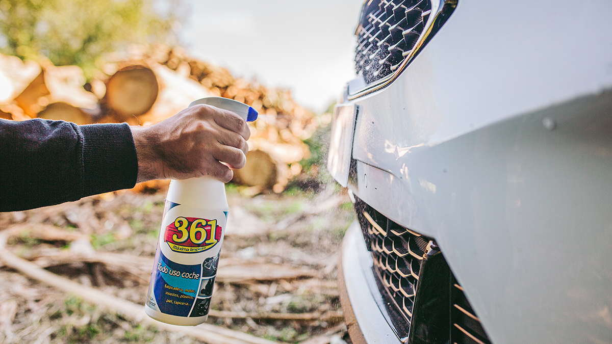 Mão a pulverizar 361 Todo Uso sobre a grelha frontal de um carro. O produto parece estar concebido para remover insetos e sujidade da superfície do veículo.