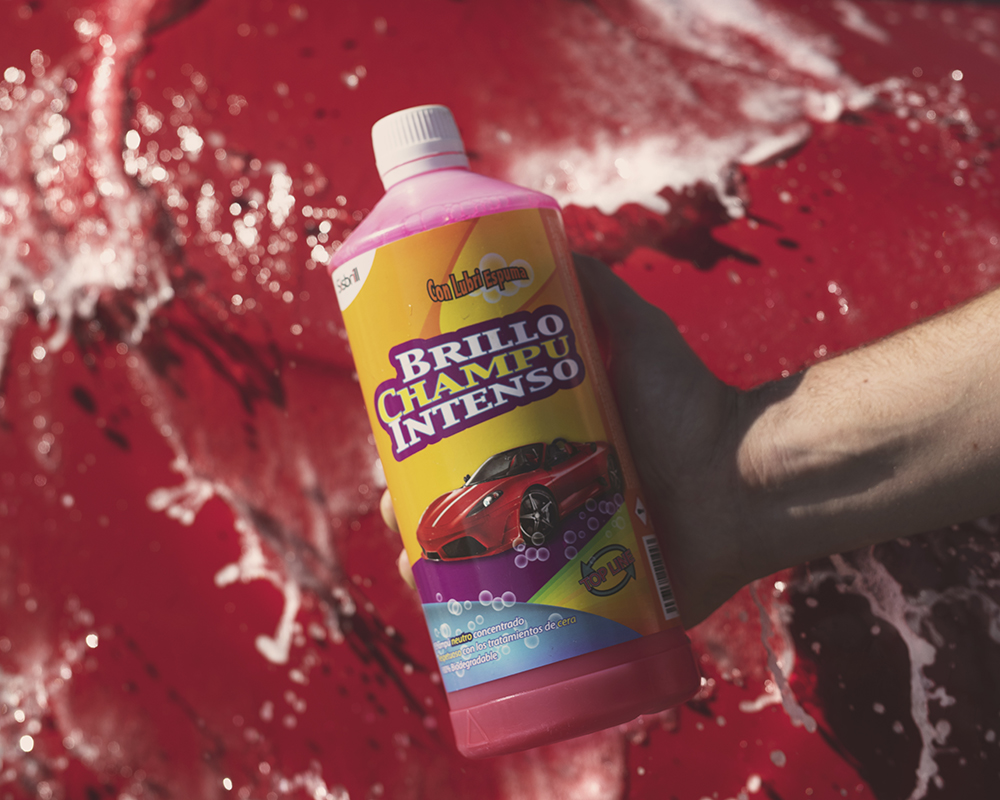 Garrafa de Champú Brillo Intenso com o capô de um carro vermelho ao fundo