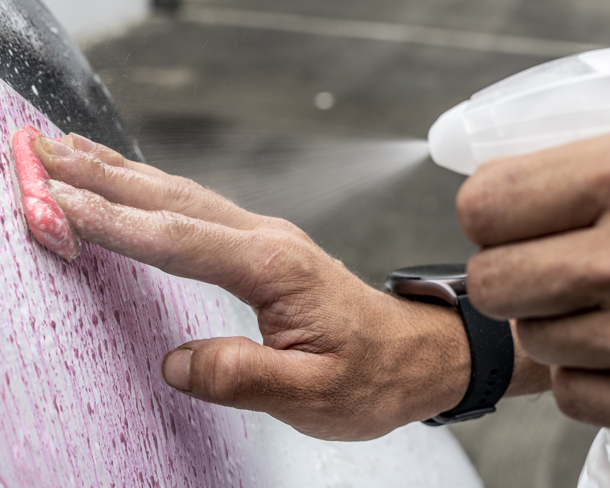 Mão de um homem a esfregar com uma claybar rosa a carroçaria de um carro