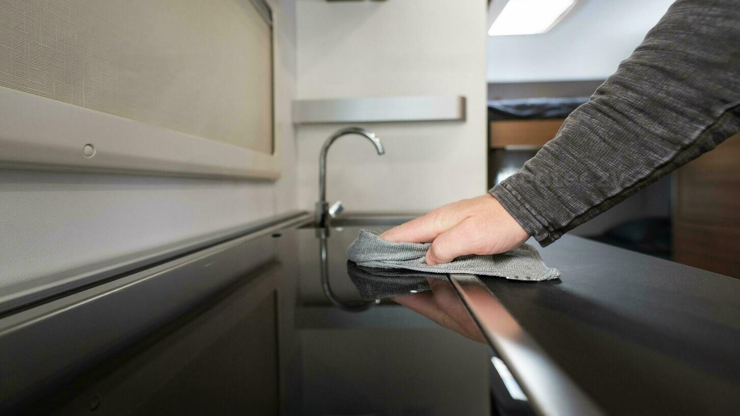 Pessoa a limpar a cozinha de uma autocaravana com um pano de microfibra