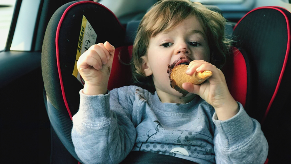 Bebé com a boca suja de chocolate na cadeirinha do carro a comer um doce