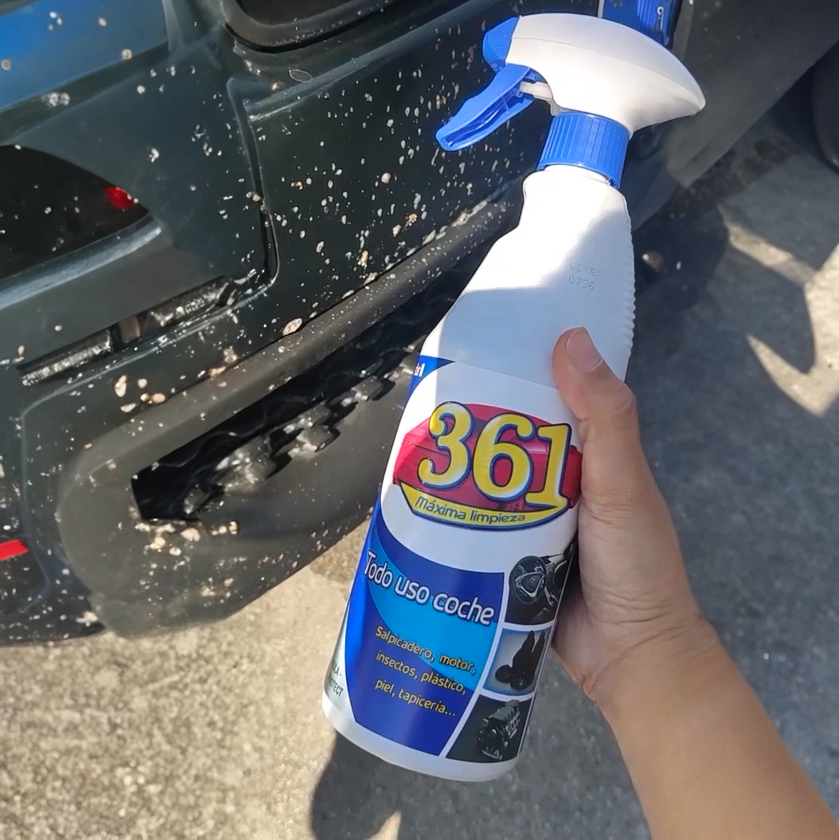 Persona sujetando una botella de 361 Todo Uso delante de la defensa de un coche llena de mosquitos