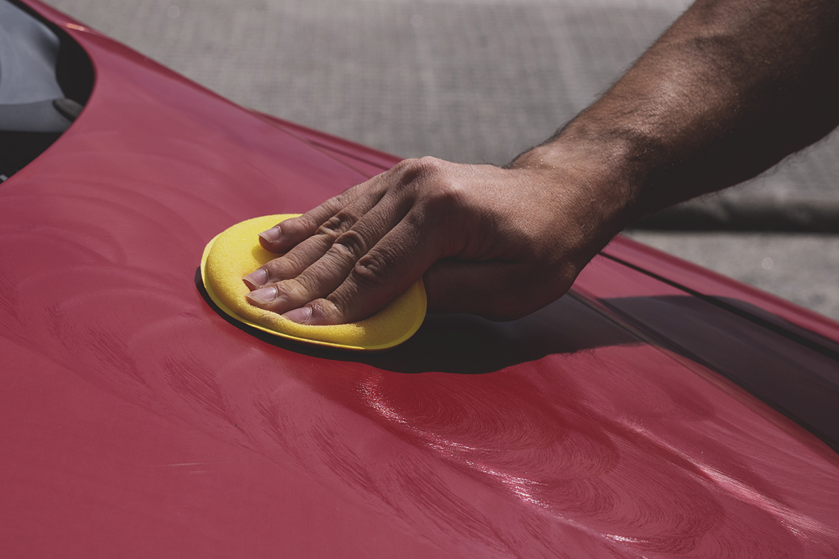 M&atilde;o de um homem com um aplicador de poliespuma amarelo sobre o cap&ocirc; de um carro vermelho