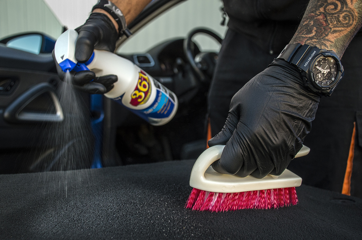 Homem com tatuagens com um 361 Todo Uso Coche numa mão enquanto esfrega com uma escova de estofos um banco
