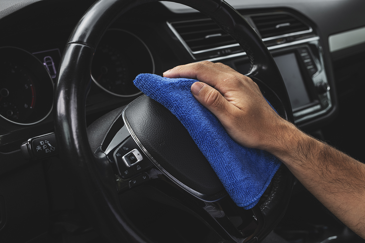 M&atilde;o de um homem com uma microfibra apoiada no volante de um carro