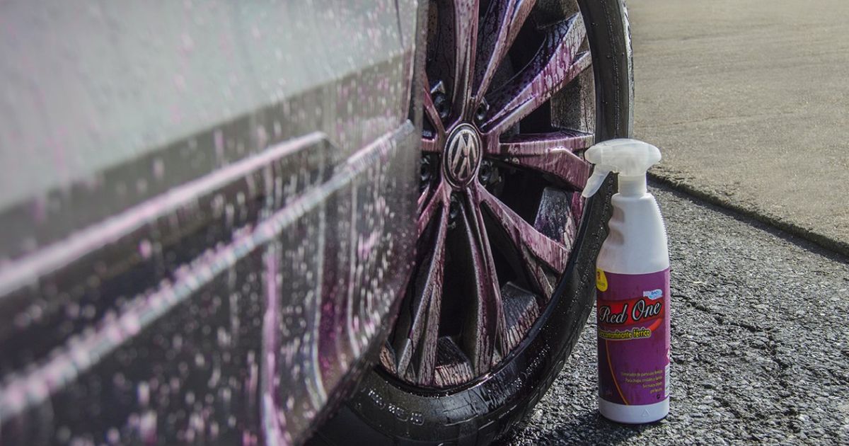 Um carro com jantes a serem limpas com Red One Descontaminante F&eacute;rrico. As jantes t&ecirc;m res&iacute;duos de l&iacute;quido roxo a escorrer, indicando que o produto est&aacute; a atuar para eliminar a contamina&ccedil;&atilde;o f&eacute;rrica.