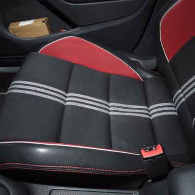 Asiento de coche deportivo en color negro con detalles en rojo y costuras blancas, mostrando un diseño acolchado con líneas horizontales grises, junto a un compartimento lateral que contiene una caja de cartón.