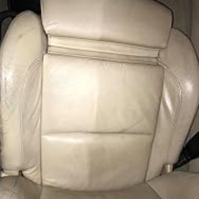 Asiento de coche de cuero beige, con una clara diferencia entre la parte limpia y la parte aún sucia, mostrando el proceso de limpieza.