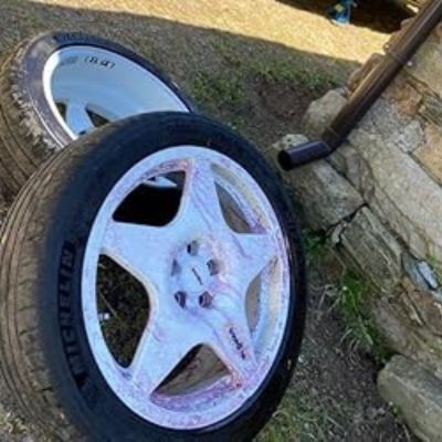 Dos llantas blancas, una de ellas con neumático Michelín, durante el procesdo de limpieza, mostrando restos de producto limpiador de color rosado sobre la superficie de las llantas.