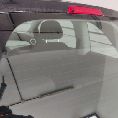 Luna trasera de un coche con gotas de agua, vista desde el exterior. El interior del coche es visible a través del vidrio, mostrando el reposacabezas y parte del asiento trasero.