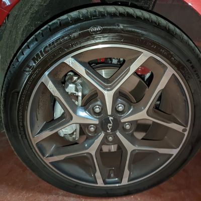 Rueda de un coche Kia con llanta de aleación de diseño deportivo y neumático Michelin, más negro en la mitad izquierda, en un coche de color rojo.